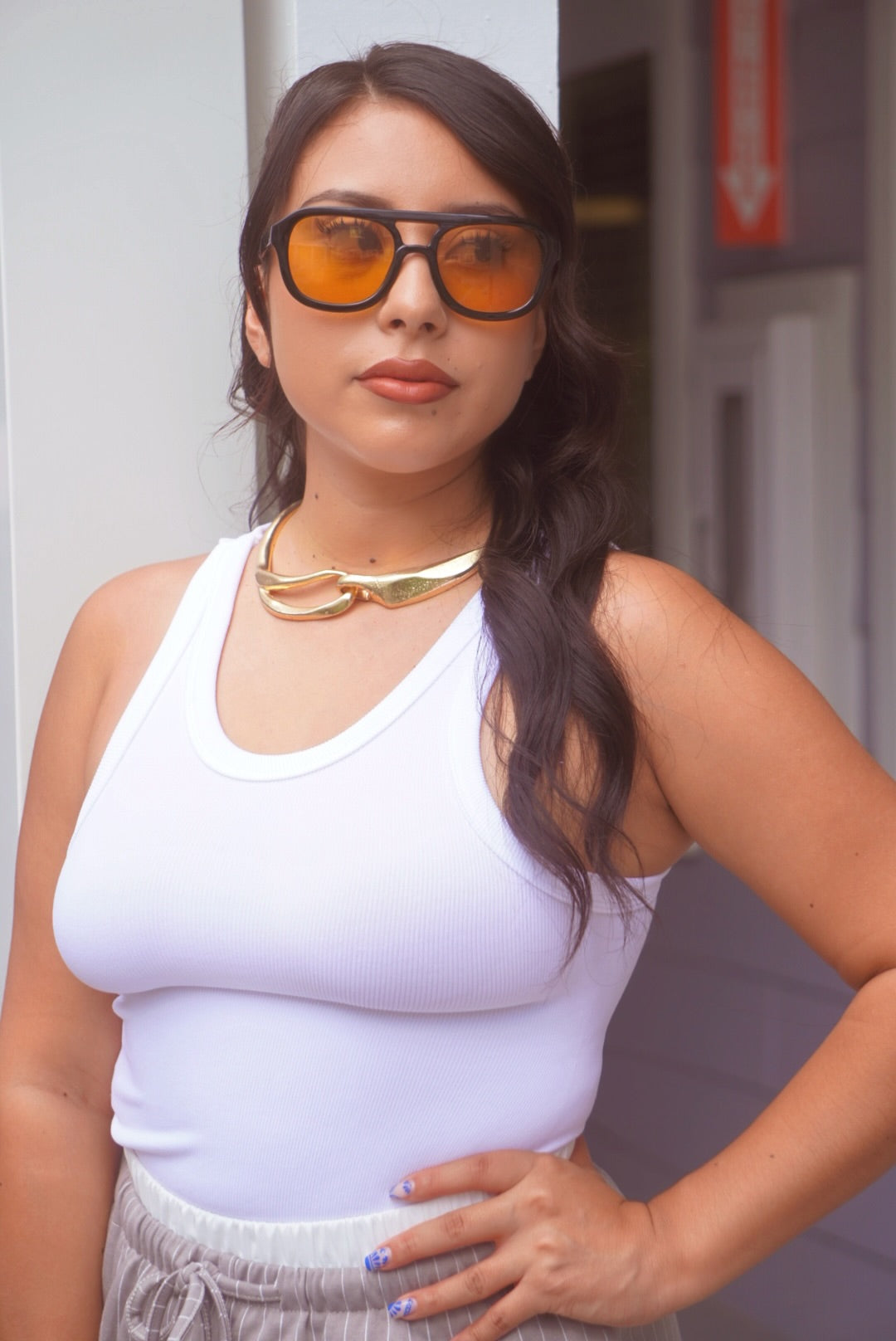 Woman wearing a white tank top and sunglasses with a blurred background