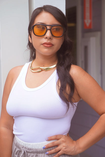 Woman wearing a white tank top and sunglasses with a blurred background